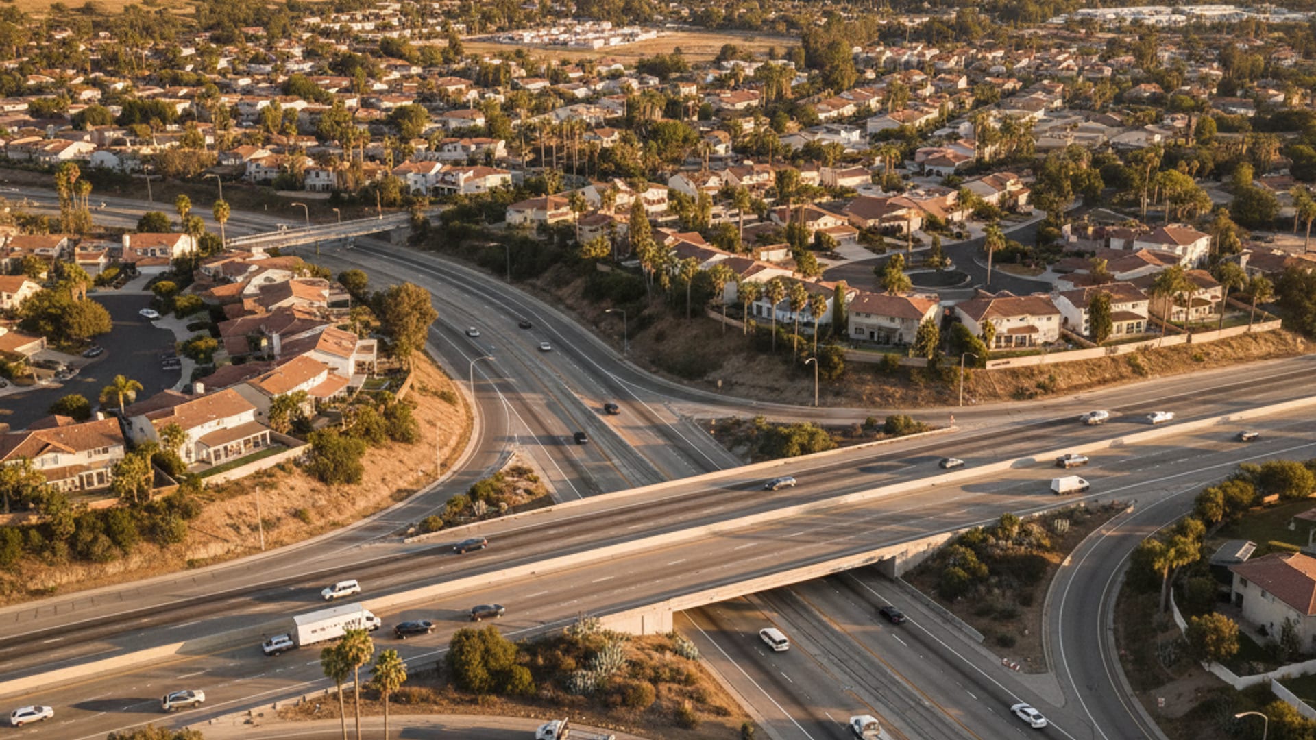 Elevated drone view of a San Diego County highway network with residential neighborhoods palm trees and hills at golden hour